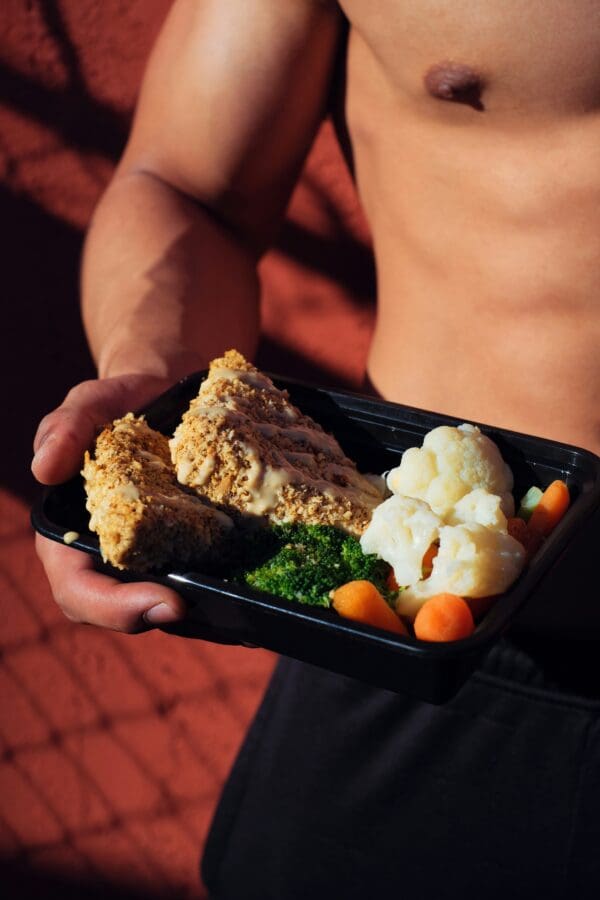 A person holding a tray of food with meat and vegetables.