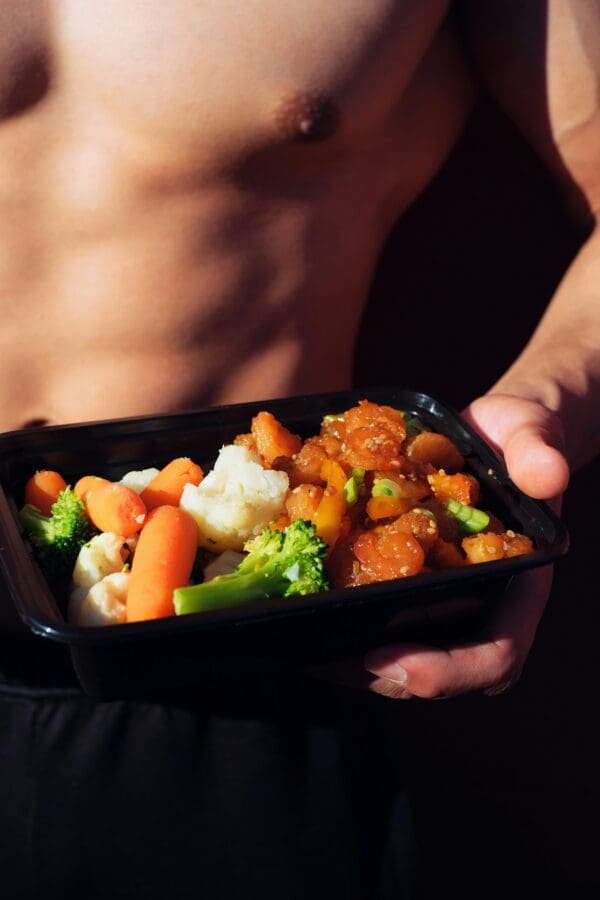 A person holding a container of food with meat and vegetables.